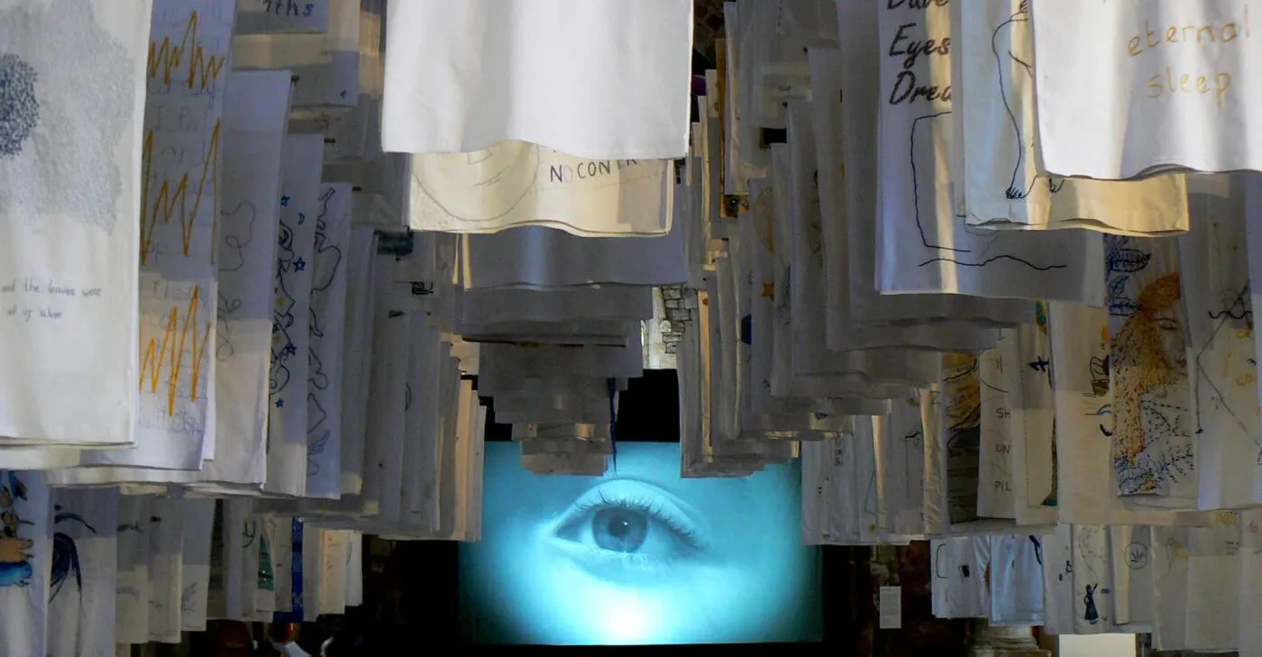 <strong>1001 Nights</strong>, installation of embroidered pillowcases with video <i>Dormez-vous?</i> behind, Susan Aldworth, 2017. Photograph by Paul Hughes.